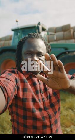 Video call. African farmer waving to the smartphone camere in front of the tractor. High quality photo Stock Photo