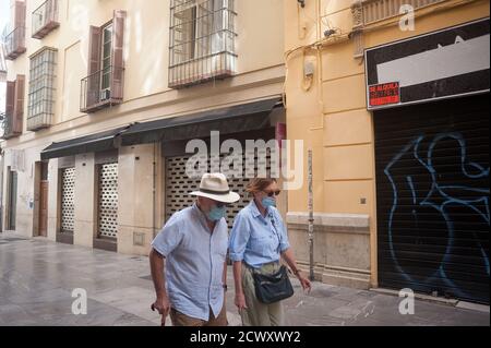 A woman and a elderly man wearing a face mask are seen walking past front closed stores. While the second wave of coronavirus disease hits Europe with special impact in Spain, many stores and shops had to closed in downtown city because of coronavirus pandemic and a decrease in sales and profits. The commercial sector in downtown represents the main sales activities to the tourists. Stock Photo