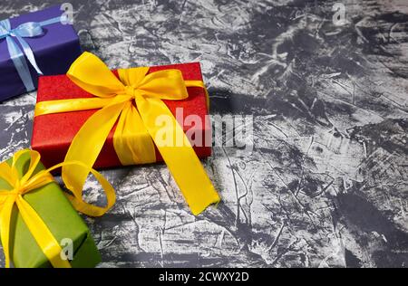 Three stylish multicolored gift boxes with bright ribbons on white and grey background. Space for text. New year concept. Stock Photo