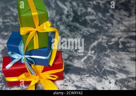 Three stylish multicolored gift boxes with bright ribbons on white and grey background. Space for text. New year concept. Stock Photo