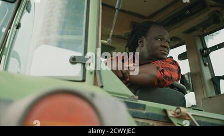 Tired young african farmer sitting in the tractor cabine and looking around. High quality photo Stock Photo