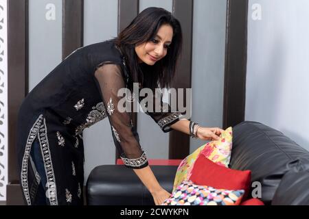 Portrait of Indian woman arranging pillows on her couch at home, doing housework. Stock Photo