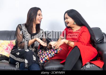 Two smiling female friends sitting on a couch at home and having a good time, laughing out happily. Stock Photo