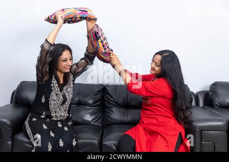 Two Indian women playfully indulge in a pillow fight while having a conversation. Two female friends having fun. Stock Photo