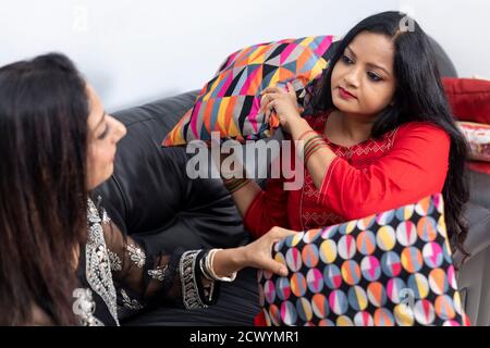 Two Indian women playfully indulge in a pillow fight while having a conversation. Two female friends having fun. Stock Photo