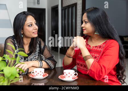 Two female friends sitting at home and having a friendly conversation, smiling women, with tea cups infront of them. Stock Photo