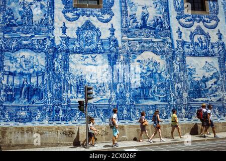 Porto, Portugal : People walk past the blue azulejo tilework by Eduardo Leite on the walls of the Capela das Almas chapel. Stock Photo