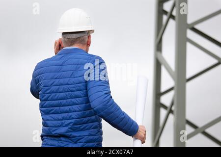 Architect or engineer talking on smart phone in front of a power pole - selective focus Stock Photo