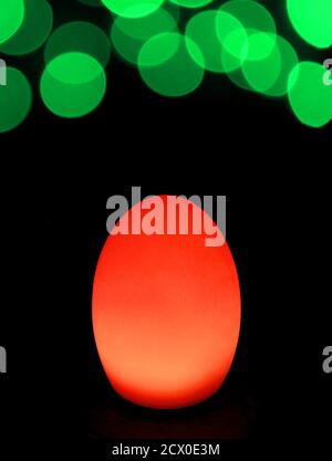Shining Vibrant Red Egg Shaped Table Lamp with Vivid Green Bokeh Light on Dark Background Stock Photo