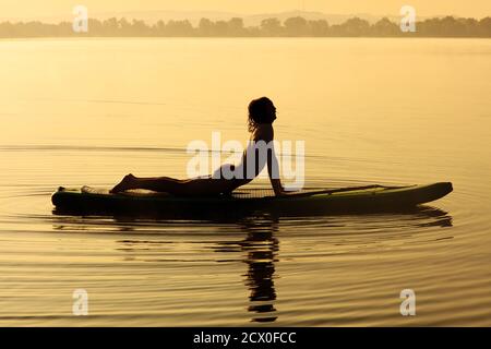 Active young guy in silhouette stretching body on sup board Stock Photo
