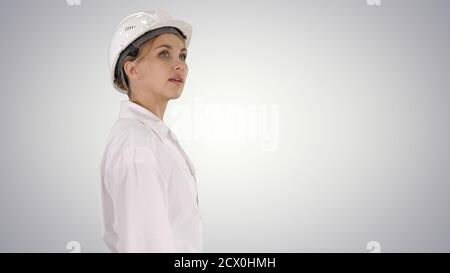 Young woman in hard hat walking and looking around on gradient b Stock Photo