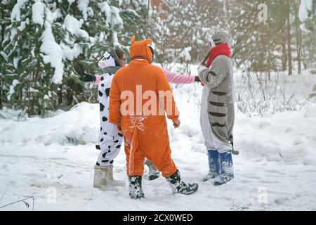 4 people, 2 girls and 2 mens in kigurumi in snow winter forest. Pajama costume pig cow kangaroo and cat. Fun with friends, walking Stock Photo