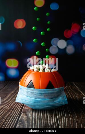 Vertical shot of a Halloween pumpkin with green jelly beans falling on it. The pumpkin has a hygienic mask to prevent Covid-19 Stock Photo