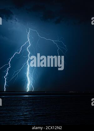 Branched lightning bolts strike down to the surface of the water at night Stock Photo