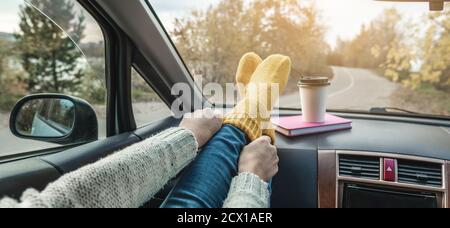 Woman in a car in warm woolen yellow socks on the car dashboard. Cozy autumn weekend trip. The concept of freedom of travel Stock Photo