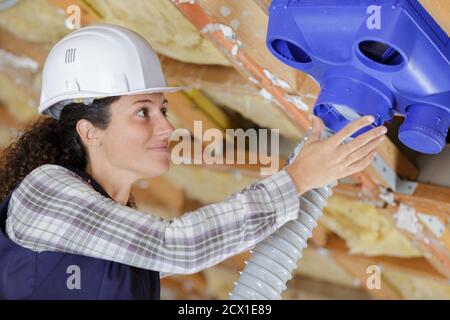 female electrician installing ventilation pipese in ceiling Stock Photo