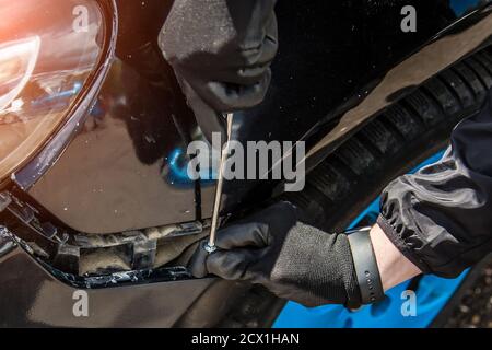 A man is trying to fix a car bumper. Screws in a screwdriver for fastening. Close-up of a hand in a black glove. Stock Photo