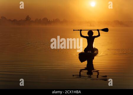 Silhouette of young sportsman swimming on paddle board Stock Photo