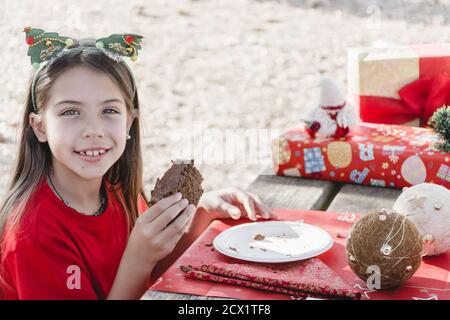 A girl celebrating a Christmas picnic in the field, wearing Santa hats, smiling, eating a cake on a decorated table Stock Photo
