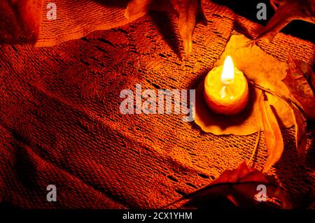 Night time still life of a single bee wax candle and autumn leaves on a orange scarf. Low key Stock Photo