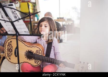 6 yr old girl practicing guitar lesson with dad in the background Stock Photo