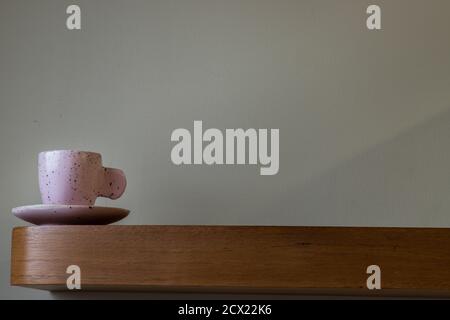 Pink ceramic mug handmade on the wooden shelf on wall of living room. Home decor. Space for text. Selective focus. Stock Photo