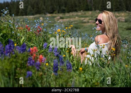 Smiling young woman sitting by flowering plants on field Stock Photo