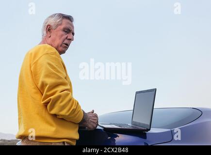 Senior man using laptop on car Stock Photo