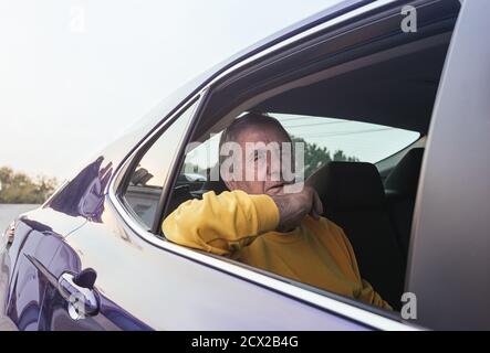 An old man sitting in the back seat of an electric car during a trip with the window open Stock Photo