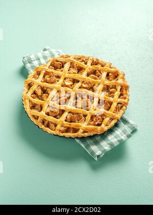 Freshly baked apple pie on a kitchen towel in bright light. Lattice crust tart with apple filling minimalist on a green colored table. Stock Photo