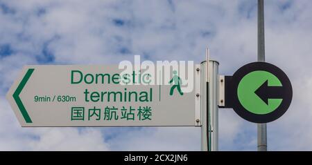 Bilingual direction sign 'Domestic Terminal' in English and Chinese at Auckland International Airport, marking the footpath between the two terminals. Stock Photo