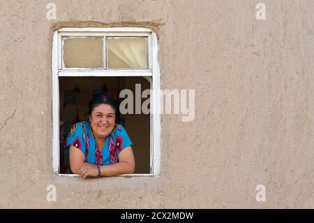 Portrait of an Uzbeki woman in local style attire at the window of her adobe walled home, Khiva, Uzbekistan Stock Photo