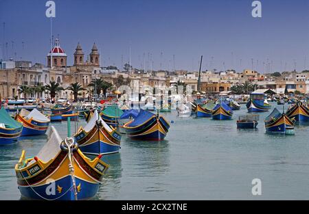 Traditional Maltese fishing boats called Luzzus moored in Marsaxlokk harbour. Our Lady of Pompeii church visible in the background Malta Stock Photo