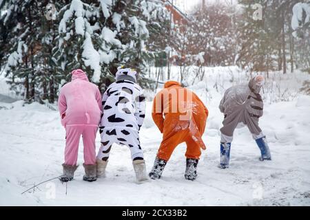 4 people, 2 girls and 2 mens in kigurumi in snow winter forest. Pajama costume pig cow kangaroo and cat. Fun with friends, walking Stock Photo