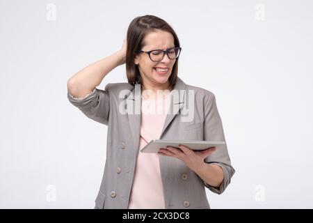 Puzzled caucasian lady hold tablet in hands trying to book tickets in internet online Stock Photo