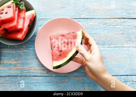 Top view fresh red watermelon slice in female hand on a pink plate on an blue rustic wood background. Stock Photo