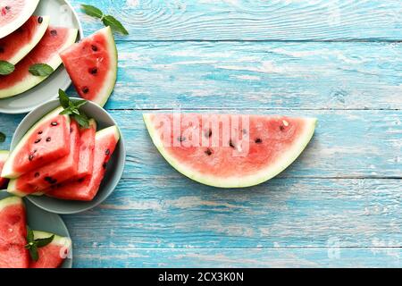Sliced ripe watermelon witn mint on a colored plates. Big slice of watermelon in center on an blue rustic wood background. top view witn copy space Stock Photo