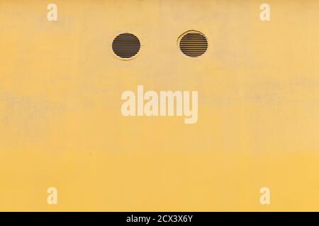 Yellow concrete wall with two round ventilation holes, abstract industrial architecture background Stock Photo