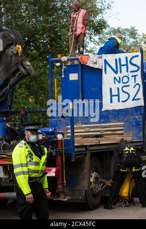 Denham, UK. 28th September, 2020. Two anti-HS2 activists with a NHS not HS2 banner, one of whom secured with a large rope around his neck, block a HGV used for works connected to the HS2 high-speed rail link. Environmental activists continue to try to prevent or delay works on the controversial £106bn project for which the construction phase was announced on 4th September from a series of protection camps based along the route of the line between London and Birmingham. Credit: Mark Kerrison/Alamy Live News Stock Photo