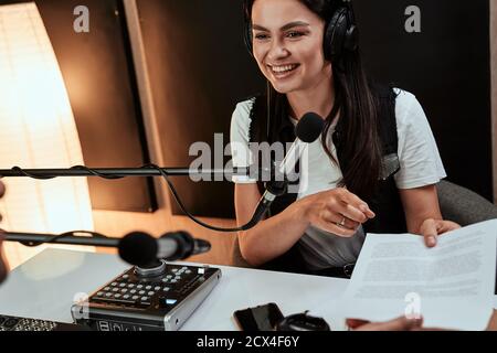 Portait of happy female radio host smiling and giving a script paper to her male colleague while moderating a live show in studio Stock Photo