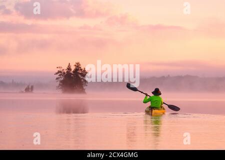 North America, Great Lakes, North Woods, Minnesota, Boundary Waters , Wilderness Canoe Area, woman in kayak at sunrise Stock Photo