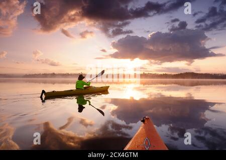North America, Great Lakes, North Woods, Minnesota, Boundary Waters , Wilderness Canoe Area, woman in kayak at sunrise on Birch lake (mr) Stock Photo
