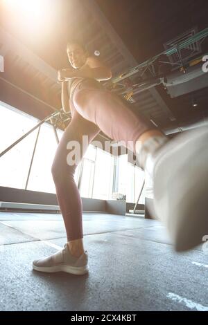 Bottom view of athletic woman in sportswear kicking with the leg while working out at industrial gym, warming up before training. Sport, wellness and healthy lifestyle Stock Photo