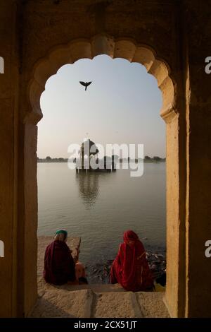 Indian women in saris feeding catfish at Gadi Sagar, Gadisar lake, Jaisalmer, Rajasthan, India Stock Photo
