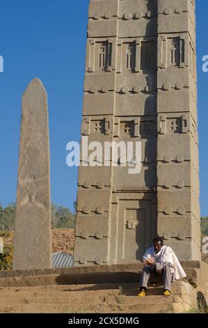 King Ezana's Stela is the central obelisk still standing in the Northern Stelae Park in the ancient city of Axum in modern-day Ethiopia. Ethiopian Pilgrim reading prayer book at base of obelisk Stock Photo