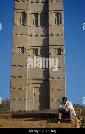 King Ezana's Stela is the central obelisk still standing in the Northern Stelae Park in the ancient city of Axum in modern-day Ethiopia. Ethiopian Pilgrim reading prayer book at base of obelisk Stock Photo