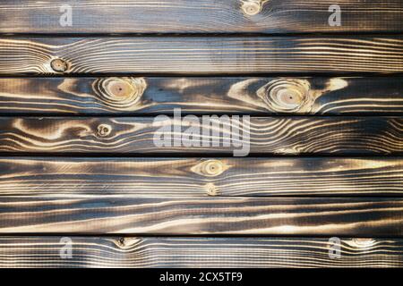 Old burnt wooden plank dark brown texture background with horizontal boards. Flat lay close-up view. Stock Photo