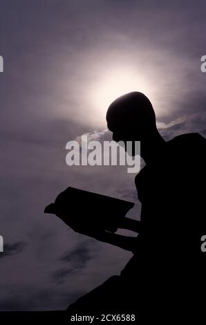 The silhouetted shape of the abbot of a local monastery, reading from his prayer book, Shan State, Burma Stock Photo