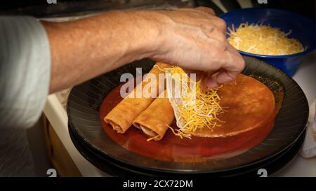 A cook adds shredded cheese to home made entomatadas being prepared in the kitchen. Stock Photo