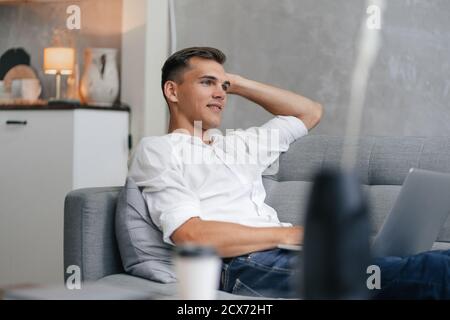 thoughtful young man with a laptop sitting on the couch. Stock Photo